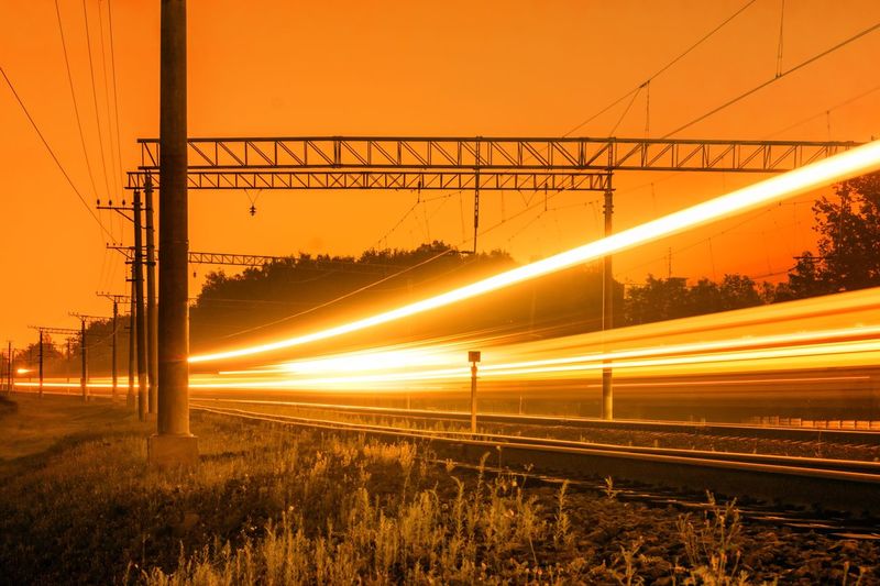 Light trails on railroad tracks against orange sky during sunset 