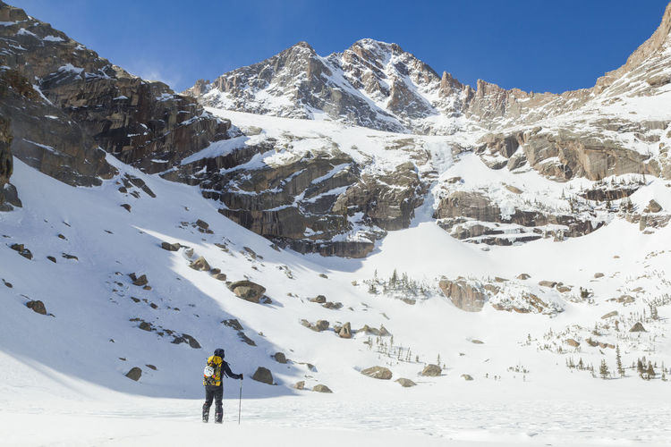 Woman hikes across frozen black lake, rocky mountain national park