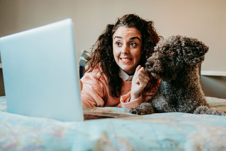 Smiling woman using laptop by dog on bed at home