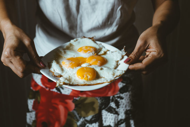 Midsection of woman holding sunny side up on plate
