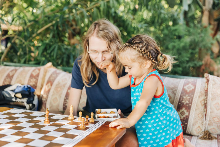 Girl standing by father arranging chess pieces on board