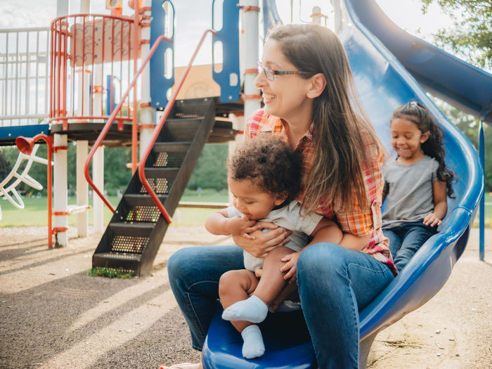 Smiling mother with kids sitting on side at park