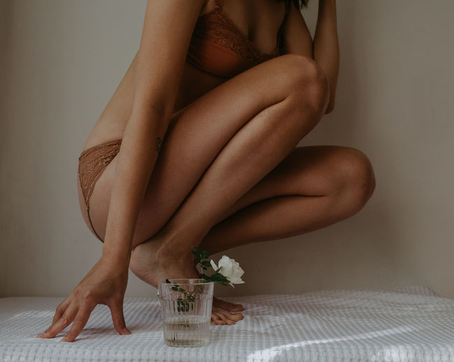 Low section of sensuous woman sitting on bed at home withthe flower