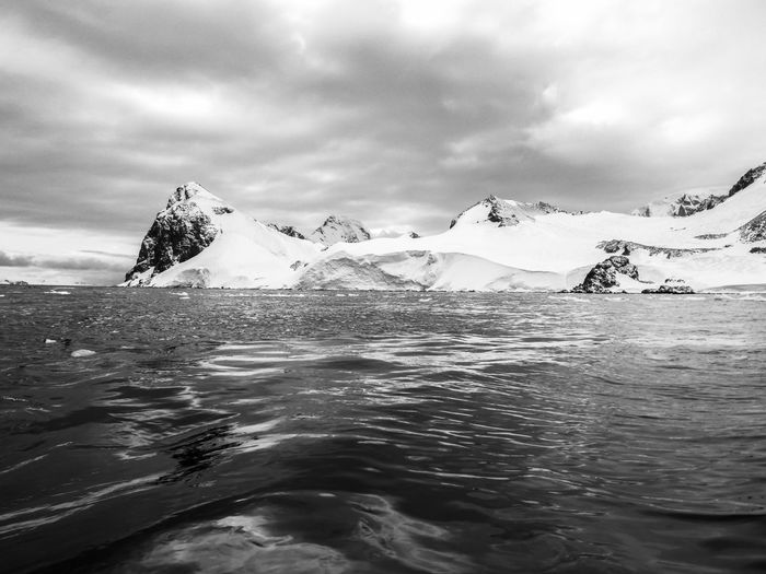 Black and white photo of waves againts snowy mountains in antarctica