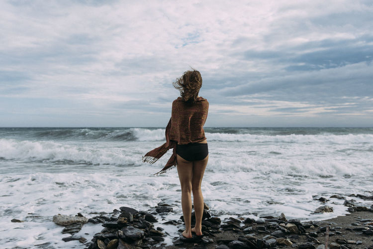 Rear view of woman standing on beach against sky