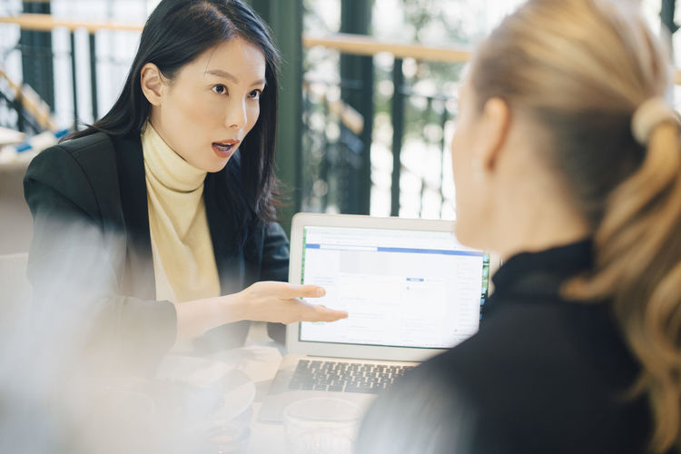 Confident businesswoman discussing over laptop with female colleague at office