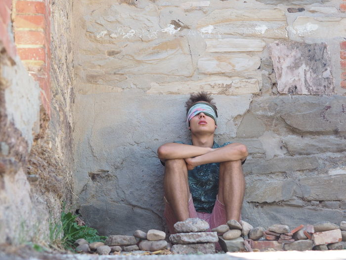 Young man with blindfold sitting against wall