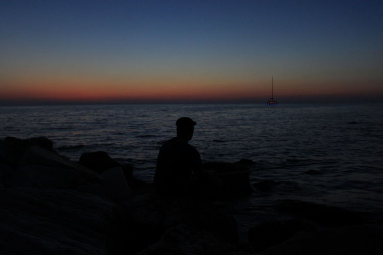 Silhouette of man sitting on beach at sunset