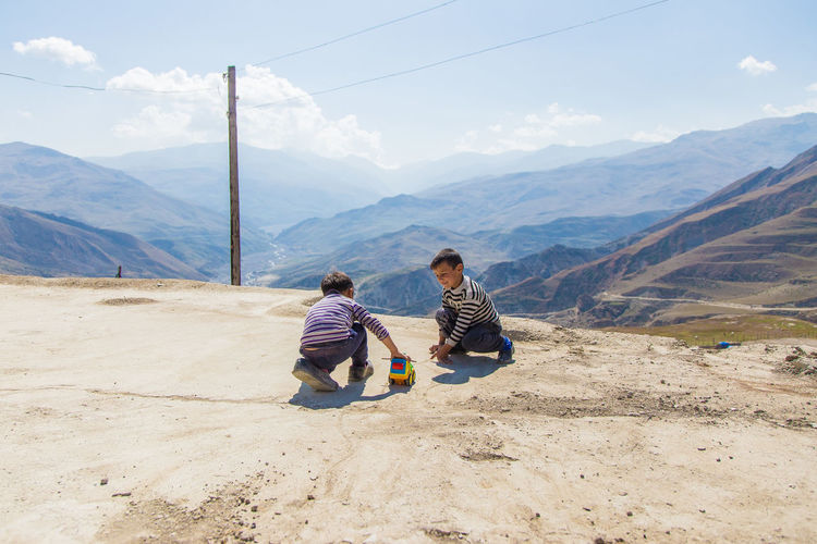 Brothers playing with toy car on mountain against sky