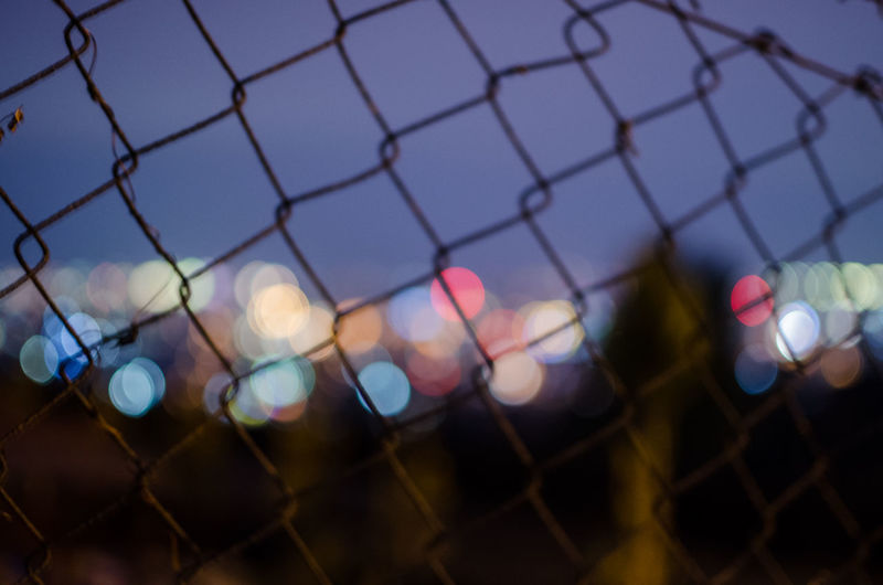 Close-up of illuminated chainlink fence against sky at sunset