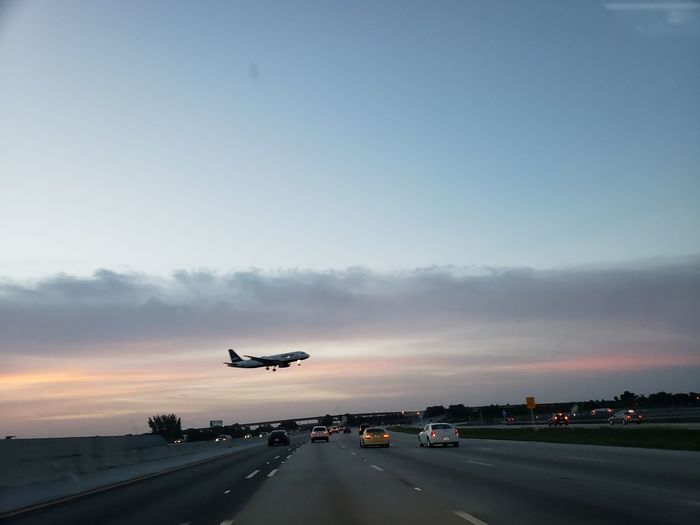Airplane flying over airport runway against sky during sunset