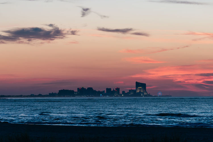 Silhouette buildings by sea against romantic sky at sunset