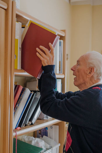 Side view of senior man keeping book on shelve