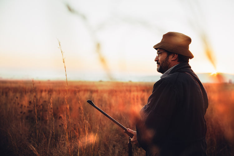 Hunter with shotgun standing in field during sunrise