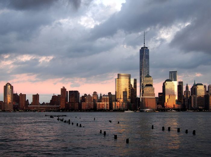 One world trade center and hudson river against cloudy sky in city