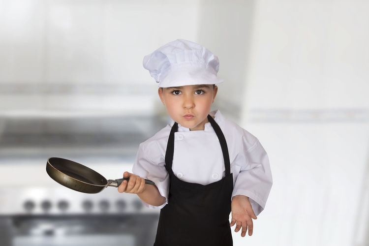 Portrait of girl wearing chef uniform standing against wall