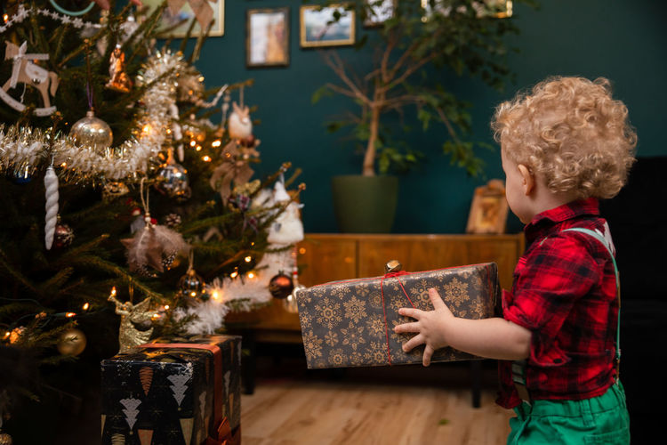 A two-year-old little boy carries a gift package on christmas day.
