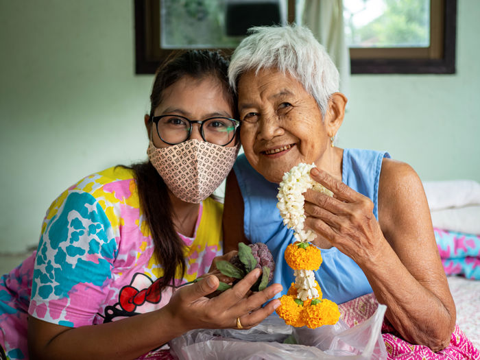 Image of a woman wearing a protective mask and a grandmother with a flower garland.