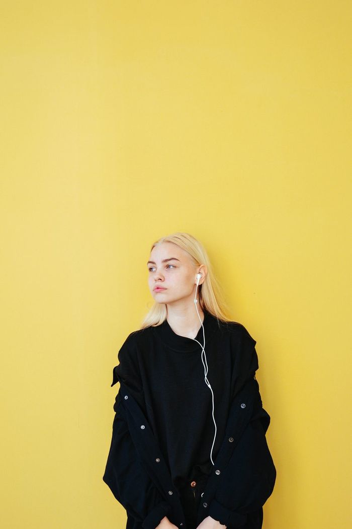YOUNG WOMAN STANDING AGAINST YELLOW BACKGROUND