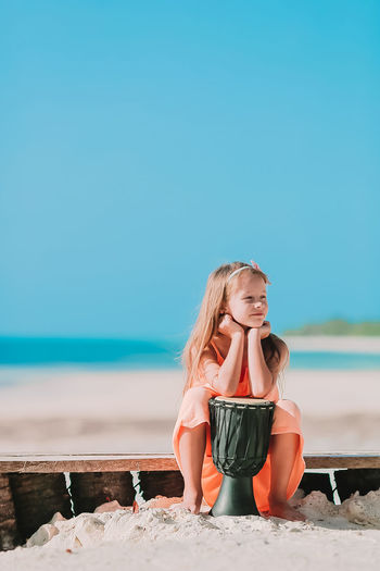 Full length of girl sitting on beach against sky