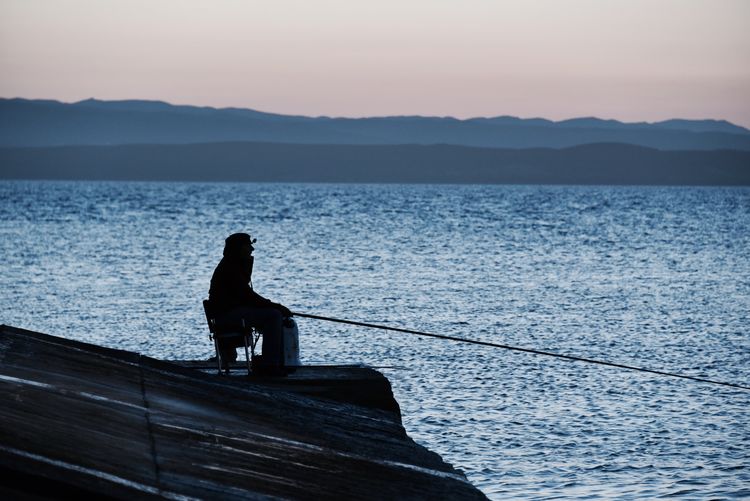 Silhouette man fishing by sea against sky during sunset