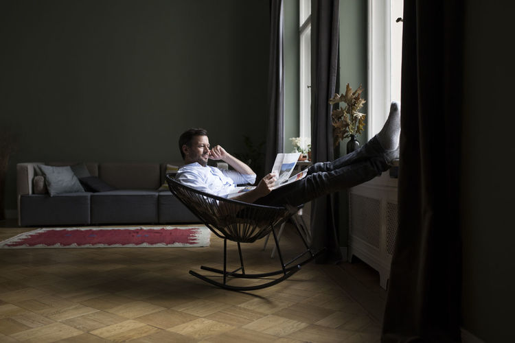 Man relaxing on rocking chair in his living room reading newspaper