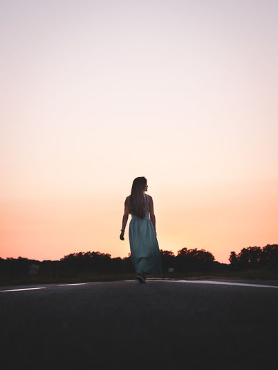 Woman standing on street against clear sky during sunset