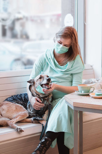 Pregnant women and her dog in medical face mask are sitting at the table in cafe. pregnancy concept. 