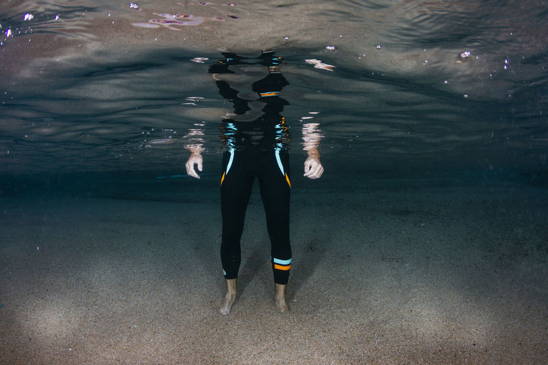 Underwater view of low section of man standing on sandy sea bottom