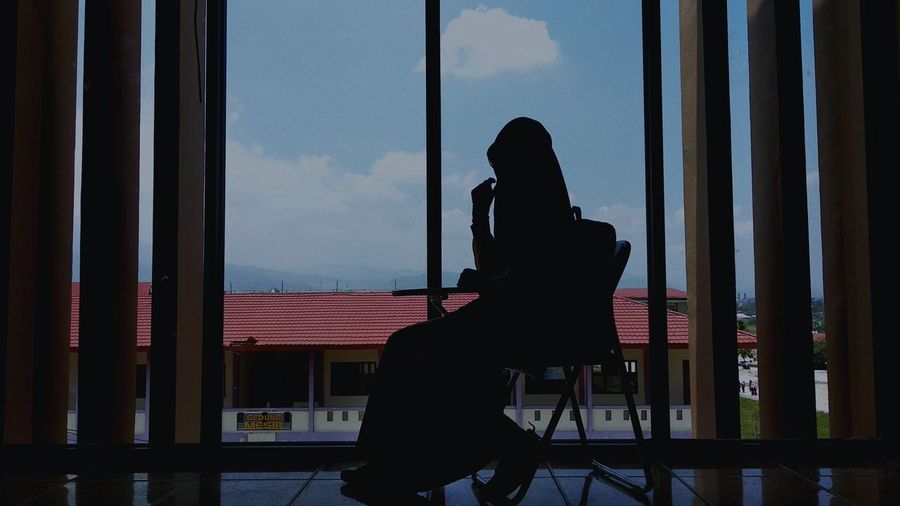 Silhouette woman standing by window against sky