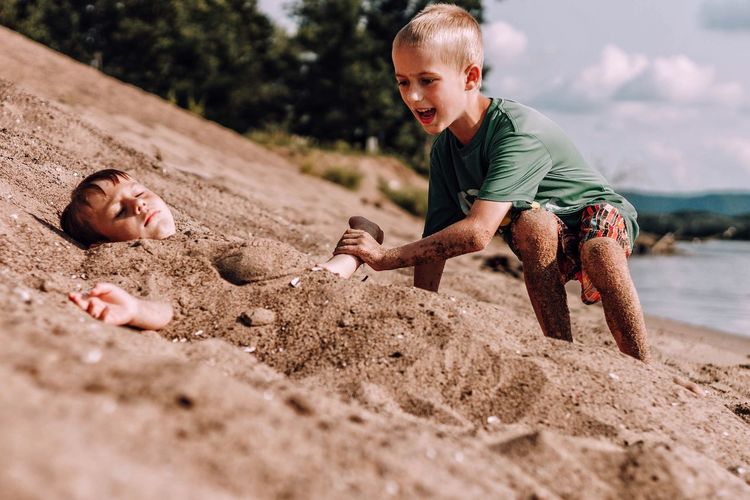 Children playing on sand at beach against sky