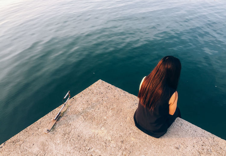 Rear view of woman relaxing on retaining wall by sea
