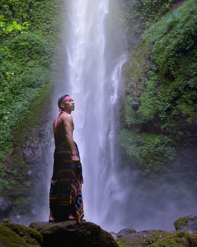 Man standing on rocks by waterfall