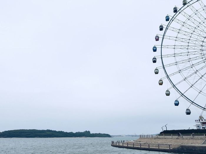Low angle view of ferris wheel by sea against sky