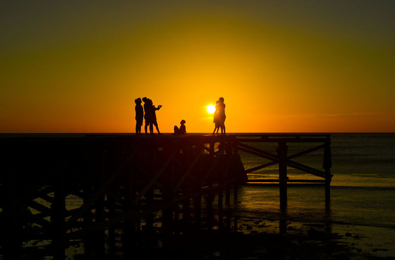Silhouette people on pier against sea during sunset