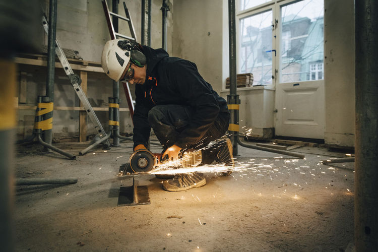 Full length of male construction worker using electric saw while cutting metal at site