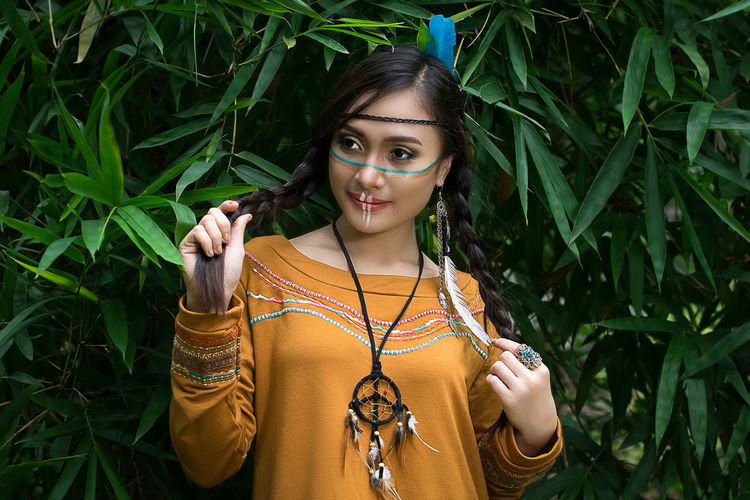 Beautiful woman in north american tribal clothing standing against plants