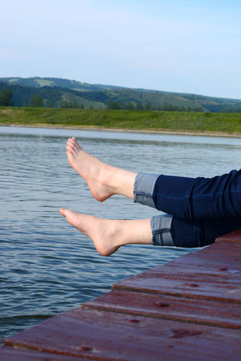 Low section of woman dangling legs while sitting on pier over lake