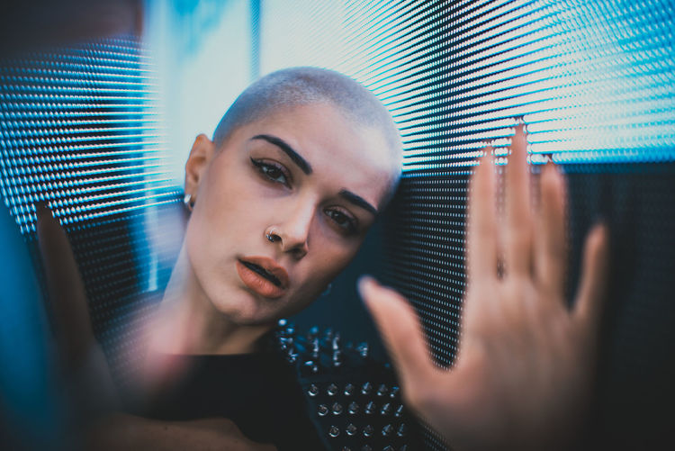 Portrait of young woman with shaved head standing against blue wall