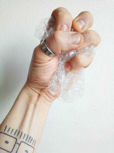 Cropped hand of man crumpling bubble wrap against white wall