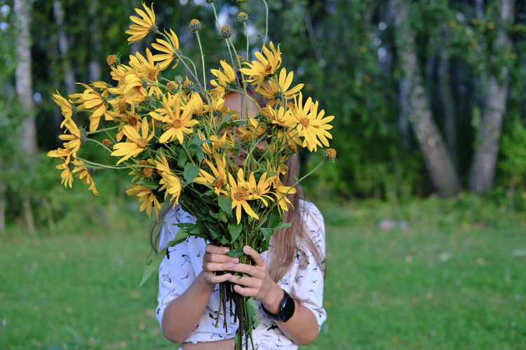 Midsection of person holding yellow flowering plant on field