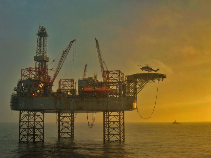 Drilling rig in sea against sky during sunset