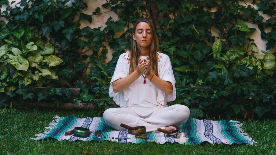 Full length of young woman meditating while sitting outdoors