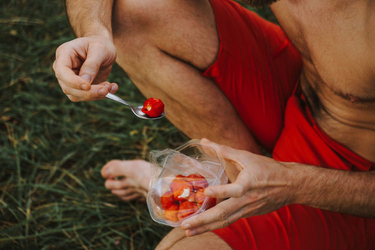 Low section of shirtless man having red fruits on field