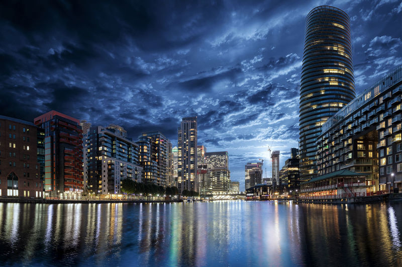 Low angle view of illuminated modern buildings by river in city against sky at night
