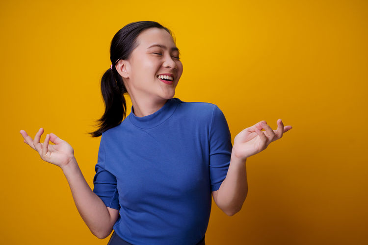 Smiling young woman standing against yellow background