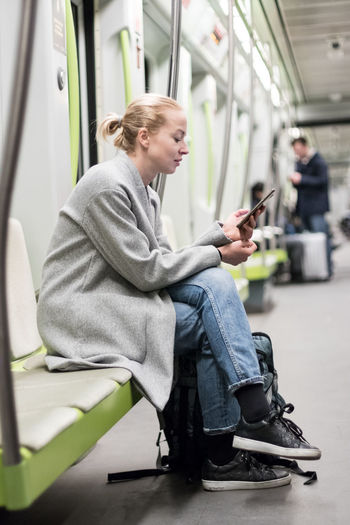Side view of woman using mobile phone sitting at subway train