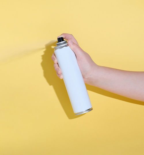 Midsection of person holding bottle against yellow background