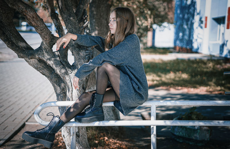Side view of woman sitting on bench against tree trunk