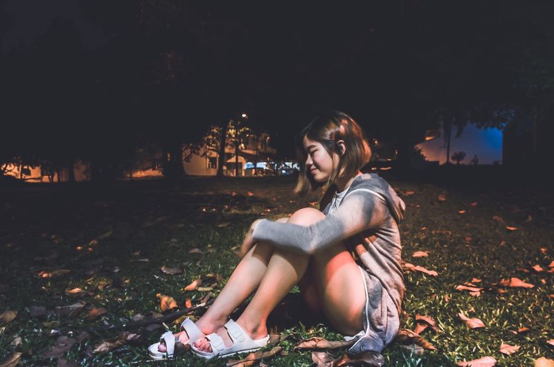Full length of young woman sitting on field at night